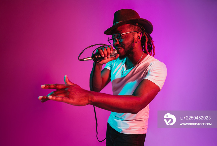 Young african-american jazz musician with microphone singing a song on purple studio background in t