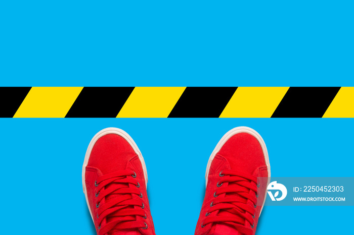 Female feet in red sneakers standing in front of a warning black-and-yellow line. Concept of the des