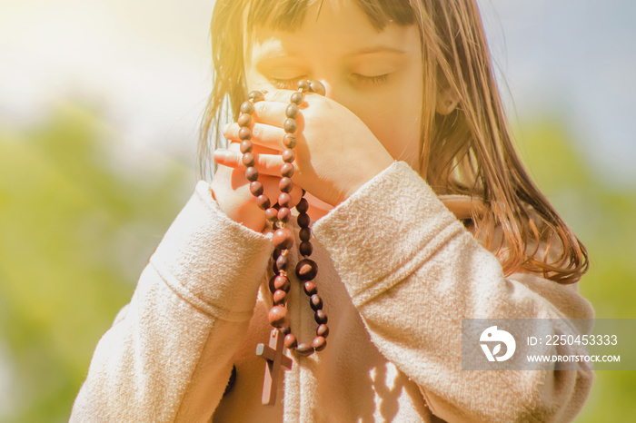 Little child girl praying with wooden rosary. Selective focus.