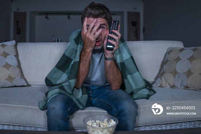 scared and funny man alone at night in living room couch watching horror scary movie or scary show i