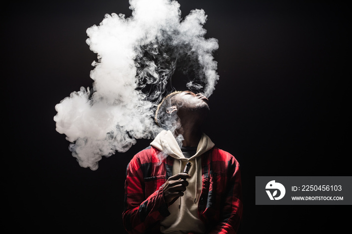 Feeling relaxed. Portrait of afro guy holding vape device and surrounded by cloud of smoke isolated 