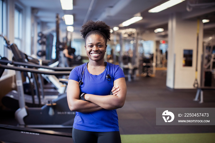 Portrait of confident smiling female athlete with arms crossed standing in gym