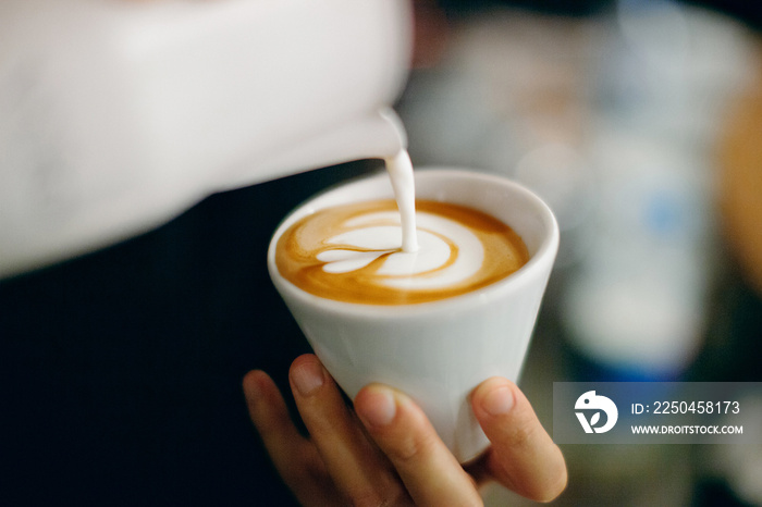 Professional barista pouring latte foame over coffee, espresso and creating a perfect cappuccino