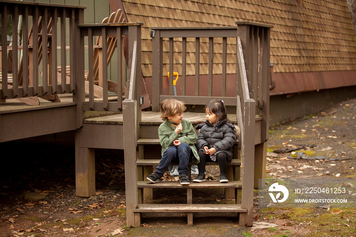 Cute friends talking while sitting on steps of house