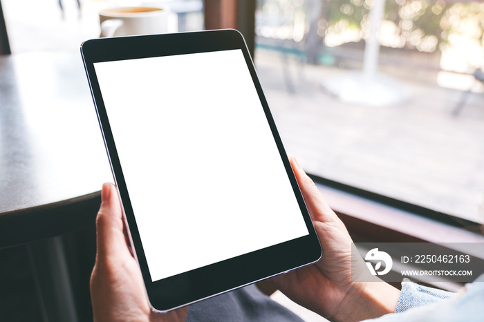 Mockup image of a woman holding black tablet with white blank screen and coffee cup on the table