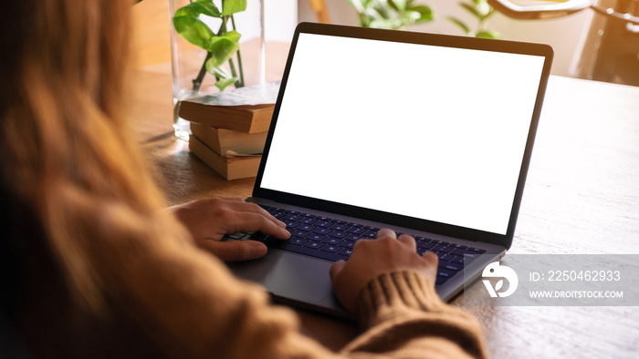 Mockup image of a woman using and typing on laptop with blank white desktop screen on wooden table