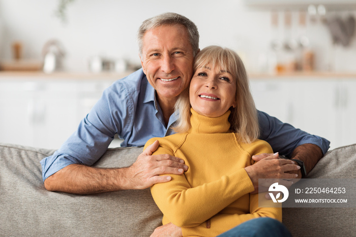 Happy Senior Couple Embracing Sitting On Sofa At Home