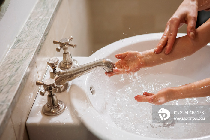 Cropped image of mother washing daughters hands in sink at home