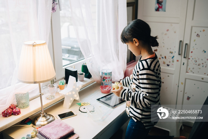 Girl playing with clay while looking at digital tablet on table in bedroom