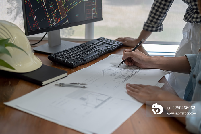 Engineers discuss a blueprint while checking information on a tablet computer in a office.