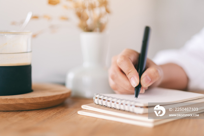 Closeup image of a woman writing on a blank notebook on wooden table