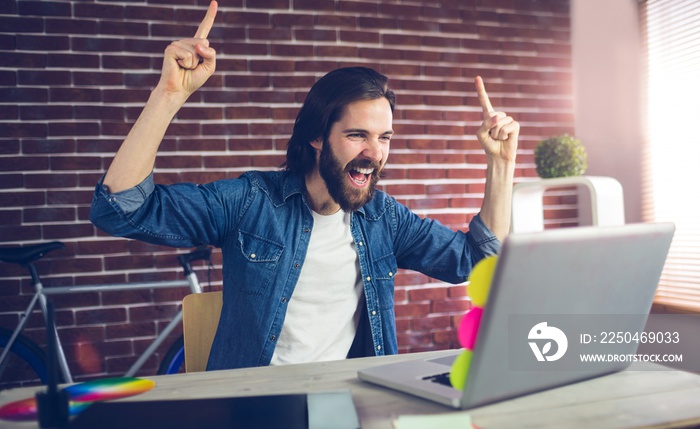 Happy creative businessman with arms raised looking at laptop