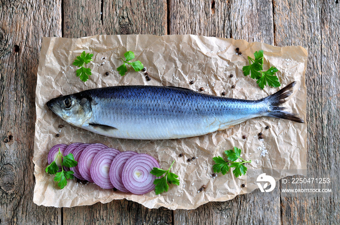 美味的腌鲱鱼，古老的木质背景上有红洋葱、盐和胡椒。乡村风格。
