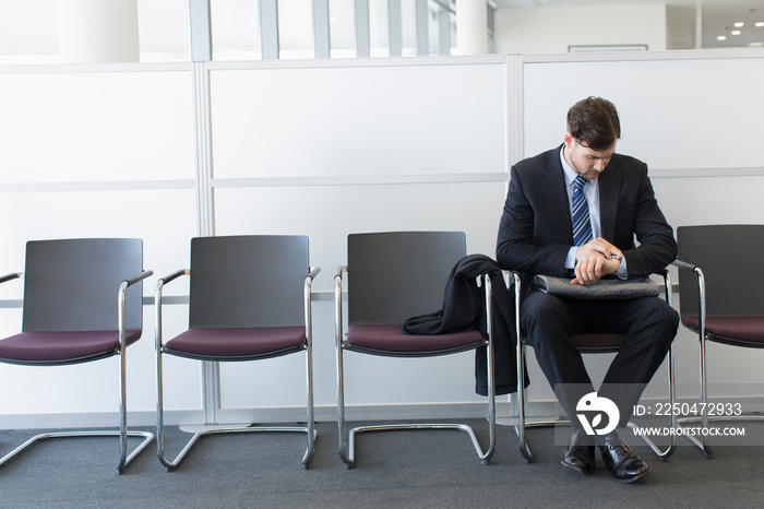 Young businessman checking time on wristwatch in office lobby