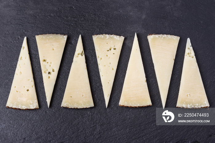 Tapa de porciones cortadas en triángulo de queso manchego curado sobre piedra oscura