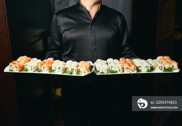 Asian cook hold a sushi roll dish. Professional chef or waiter with sushi food dish on plates in res