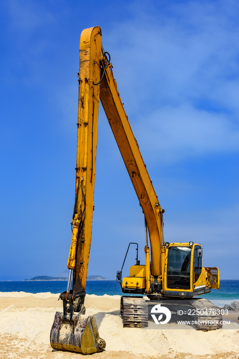 阳光明媚的海滩上，黄色的挖掘机驾驶室和手臂覆盖着沙子