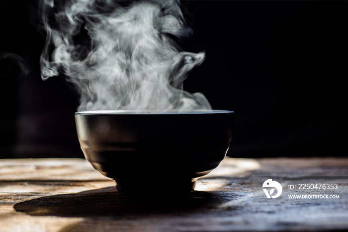 Steam of hot soup with smoke wood bowl on dark background.selective focus