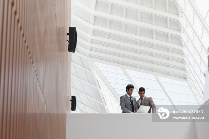 Businessmen using laptop in modern office atrium