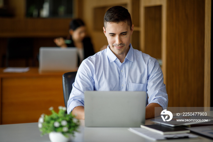 Smiling businessman working on a laptop computer in a modern office,doing finances, accounting analy