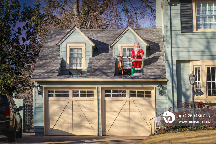 Two car garage of upscale house with plastsic santa and deer displayed by upstairs windows in evenin