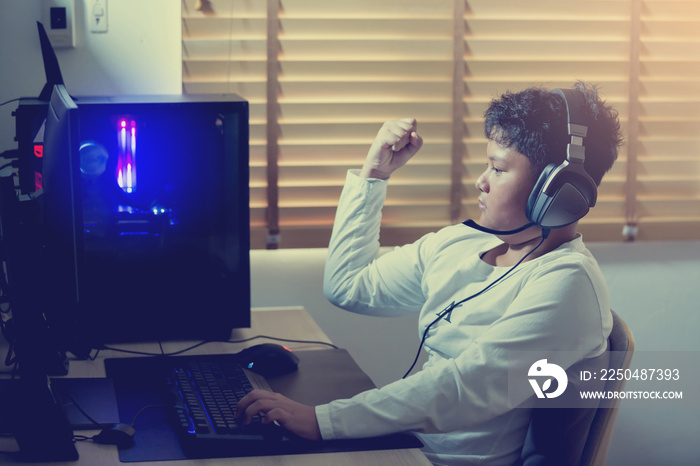 Asian boy gamer playing games on computer in the room at home, wearing headphones and using backlit 