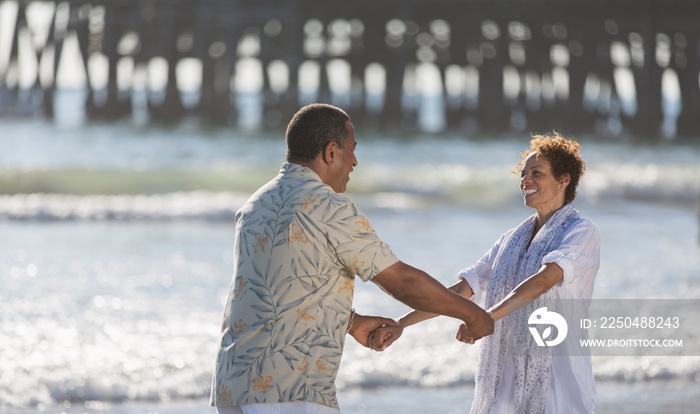 Happy active senior couple holding hands on sunny ocean beach