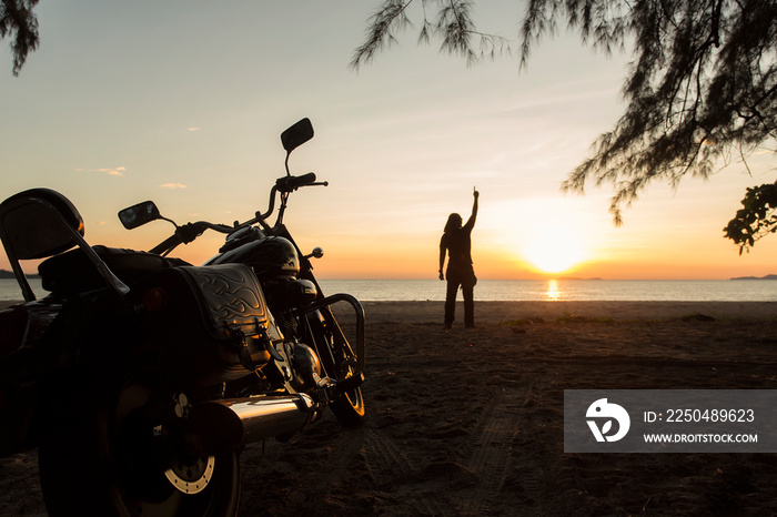 The young man stood on the beach. With a motorcycle parked He raised his hand to the sky. As if he h