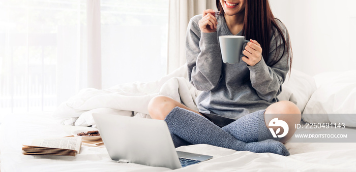 Young smiling happy beautiful asian woman relaxing using laptop computer and drinking coffee in the 