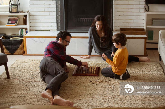 Woman looking at son playing chess with father in living room at home