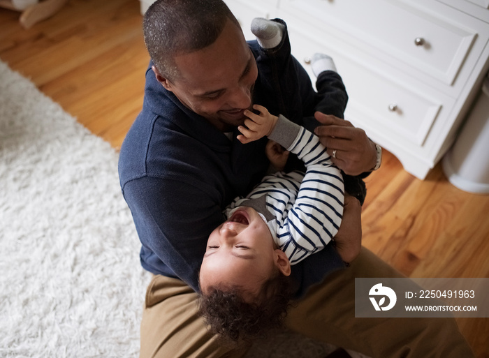 High angle view of father carrying cute happy son while sitting on rug at home