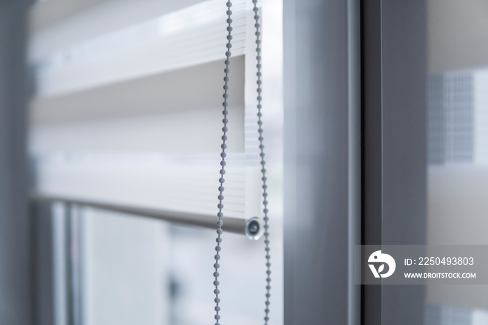 Details of white fabric roller blinds on the white plastic window in the living room. Close up on ro