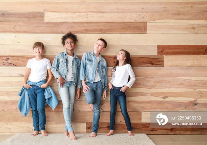 Stylish children in jeans clothes near wooden wall