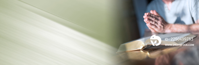 Man praying hands on a bible; panoramic banner