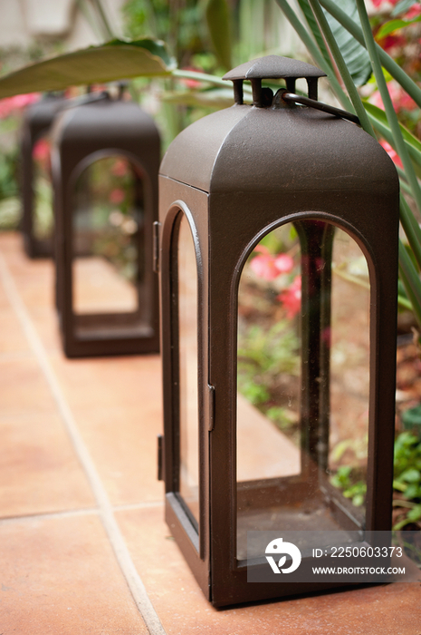 Close-up of empty lanterns in a row on tiled floor by plants