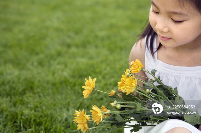手捧花朵的小女孩坐在草地上