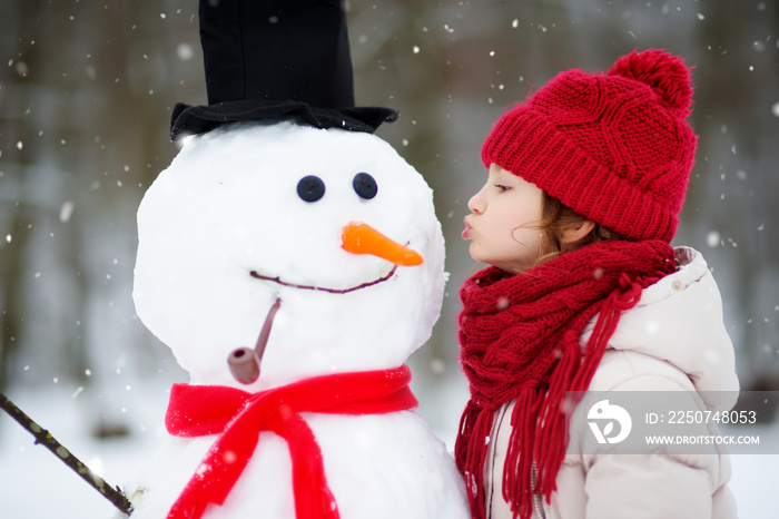 可爱的小女孩在美丽的冬季公园堆雪人。可爱的孩子在雪地里玩耍。