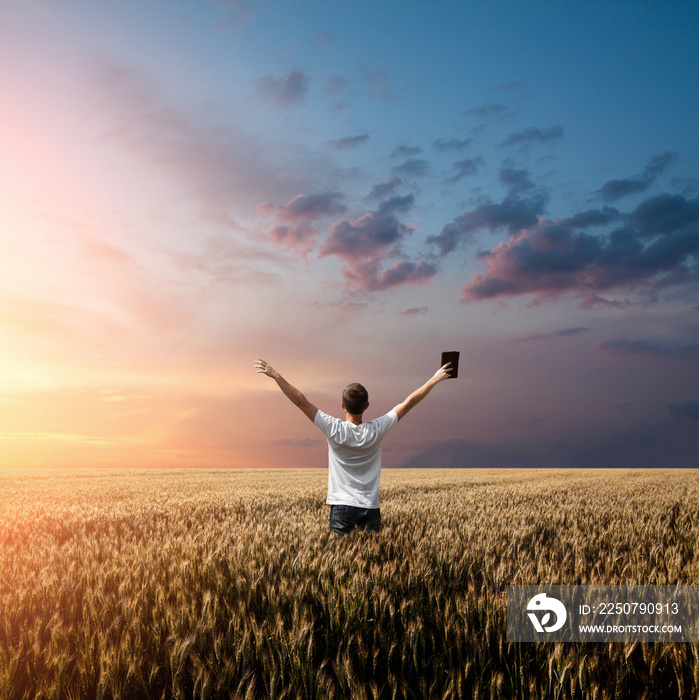 man holding up Bible in a wheat field