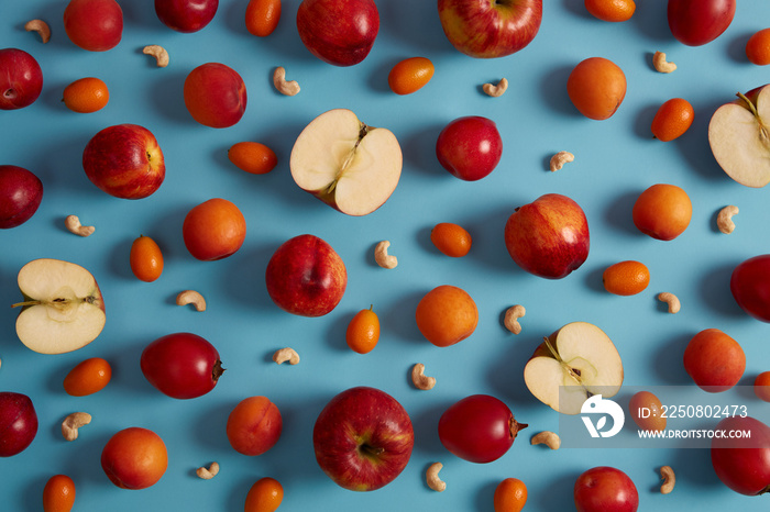 上图为蓝色背景上的红色成熟苹果、桃子、番茄、金橘和营养腰果