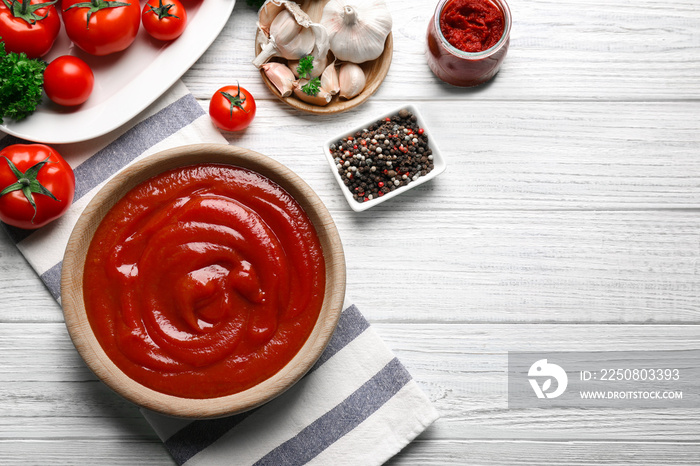 Delicious ketchup in bowl with ingredients on wooden background, top view