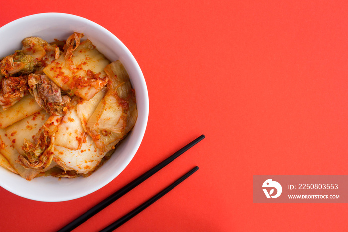 Kimchi in the white plate and black chopsticks on the red  background.Top view.Copy space.