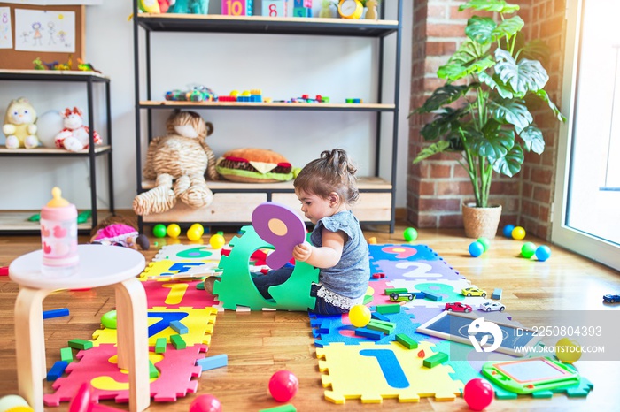 Beautiful toddler sitting on the floor playing with building blocks toy at kindergarten