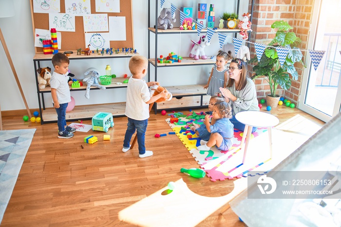 Beautiful teacher and group of toddlers playing around lots of toys at kindergarten