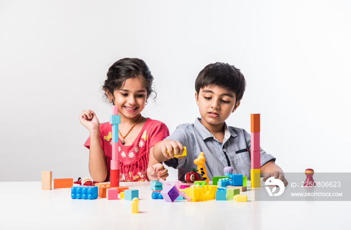 Indian cute kids playing with colourful plastic toys or blocks against white background