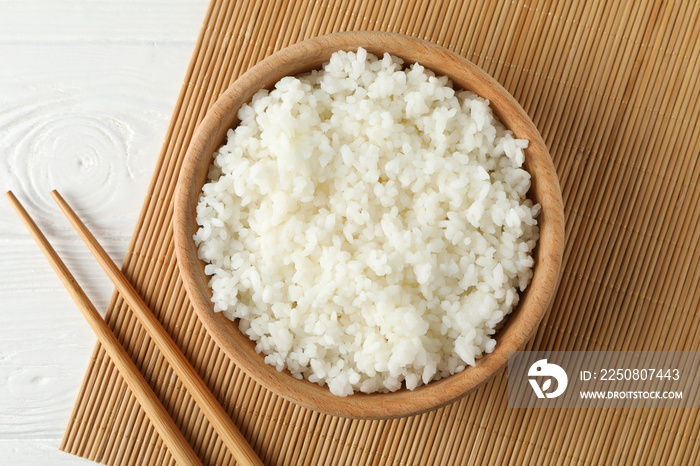 Bowl with boiled rice and chopsticks on wooden background, top view