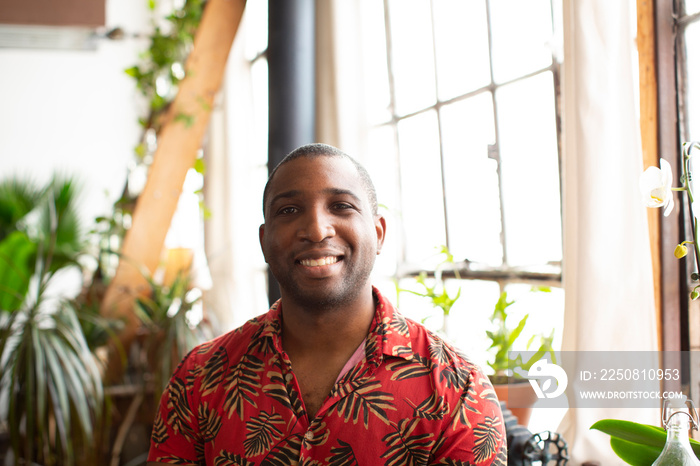 Portrait of happy man with shaved head sitting against window at home