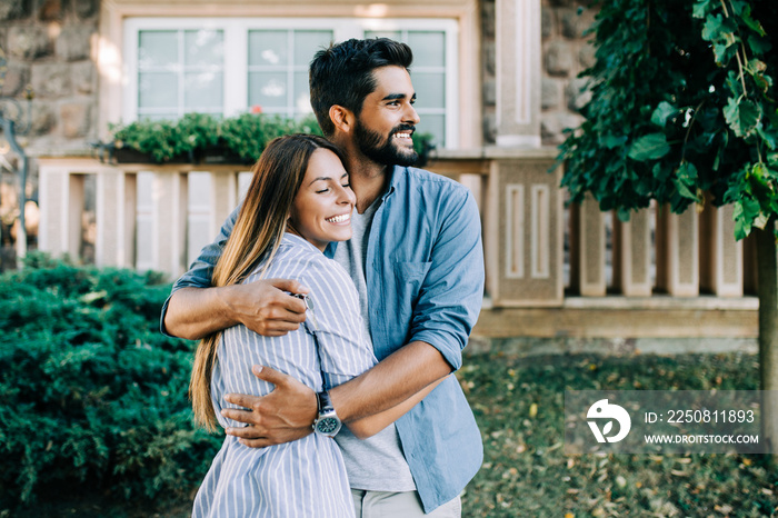 Beautiful happy young couple standing together outside in front of their new home.