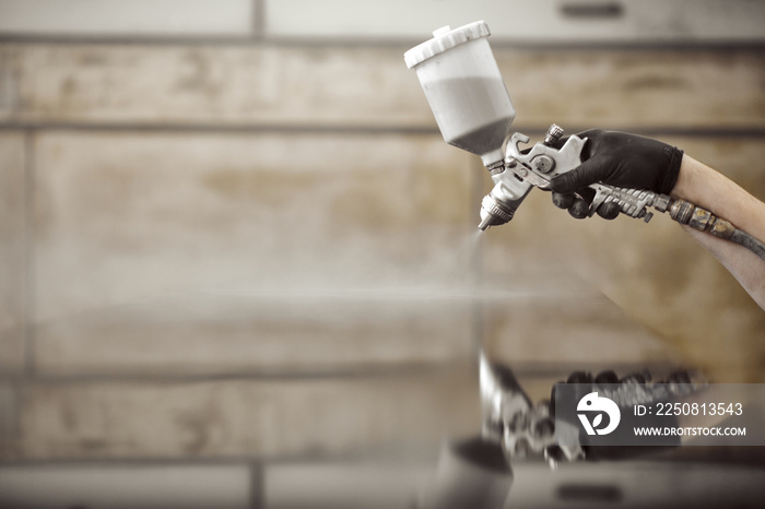 Hands of industrial worker applying spray paint gun with a wooden furniture the workshop background.