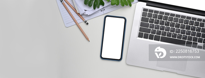 Top view of white office desk with mock up smart phone with blank screen and laptop computer.