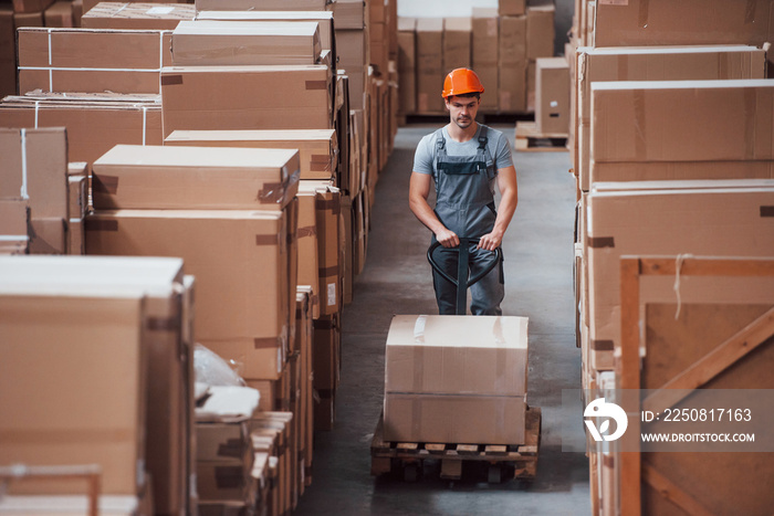 Young male worker in uniform is in the warehouse with pallet truck